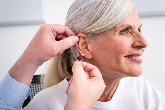 Ältere Frau bekommt modernes Hörgerät vom Hörgeräteakustiker ins Ohr eingesetzt.